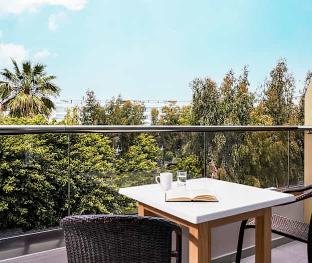 En balkon med et bord og stole, udsigt over træer og himmel. (AI-genereret tekst)