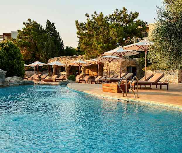 Udendørs swimmingpool med liggestole og parasoller ved siden under skyggefulde træer. (AI-genereret tekst)