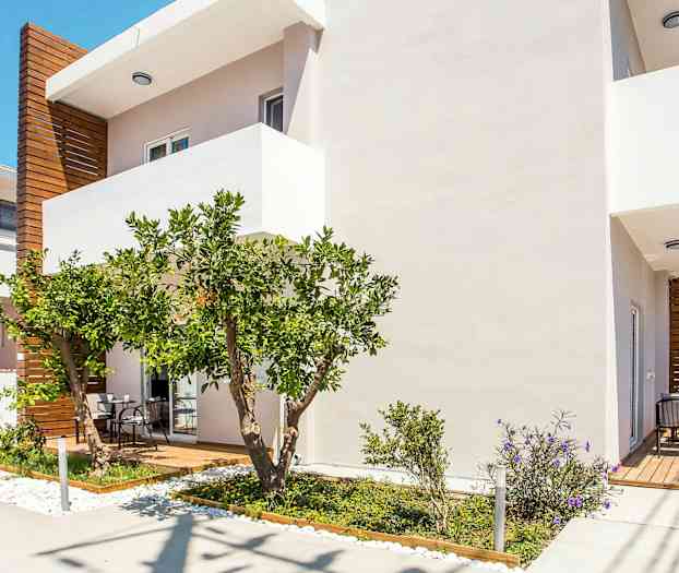 Hvid bygning med trædetaljer, en terrasse og frodig have. (AI-genereret tekst)