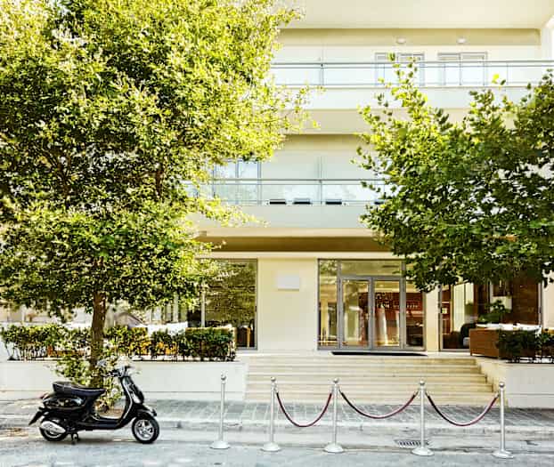 En bygning med træer i forgrunden og en parkeret scooter foran indgangen. (AI-genereret tekst)