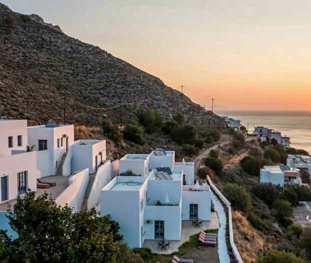 Hvidmalede huse på en skråning ved solnedgang, med udsigt over havet. (AI-genereret tekst)