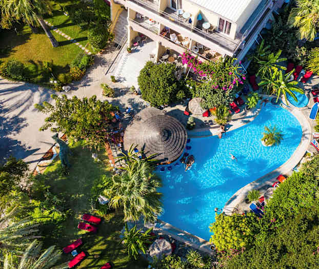 Udsigt ovenfra af et poolområde omgivet af grønne omgivelser og et hotel. (AI-genereret tekst)