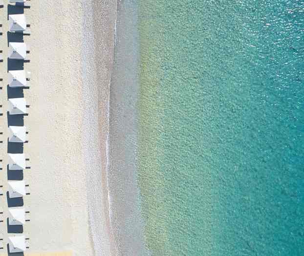 Luftfoto af strand med parasoller og klart turkis vand. (AI-genereret tekst)