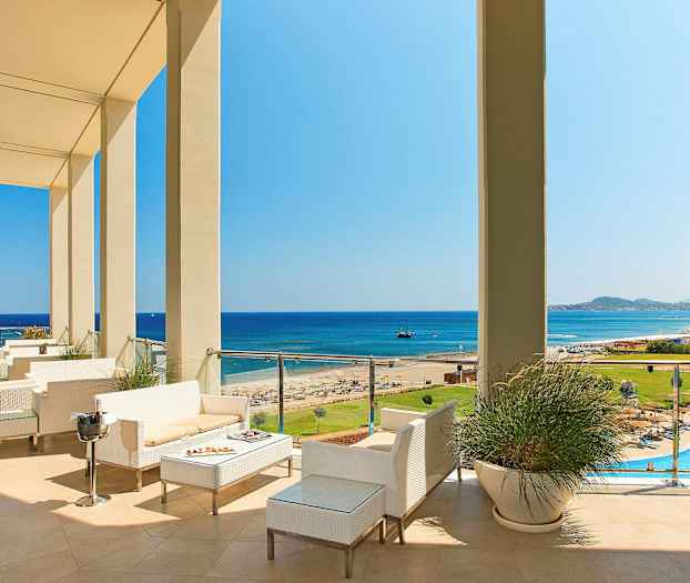 Udsigt over en terrasse med siddepladser, mod stranden og havet. (AI-genereret tekst)