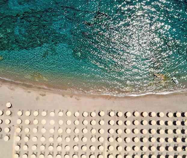 Strand med parasoller set ovenfra nær klart vand. (AI-genereret tekst)