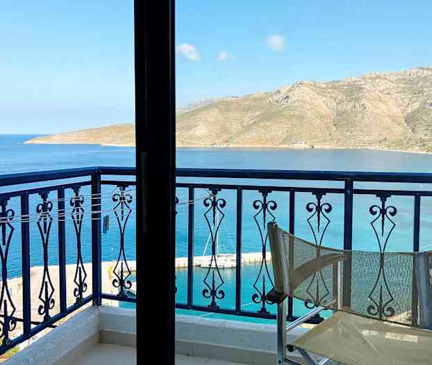 Udsigt fra en altan med en stolsryg i forgrunden, mod havet og bjerge i det fjerne. (AI-genereret tekst)