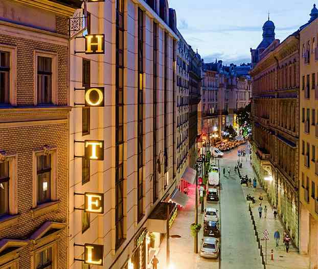 Billede af en bygade om aftenen med et hotelskilt på en bygning. (AI-genereret tekst)