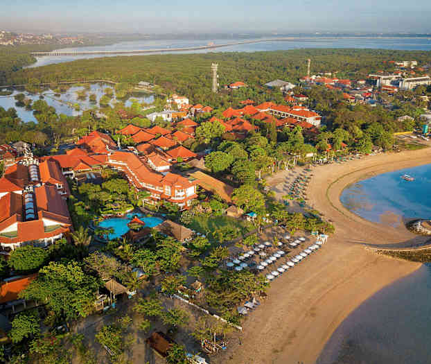 Luftfoto af et strandhotel omgivet af tropisk vegetation, stranden med liggestole og havet. (AI-genereret tekst)