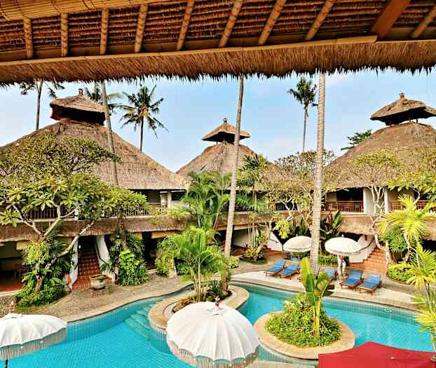 Et feriested med en pool omgivet af palmer og stråtækte bygninger. (AI-genereret tekst)