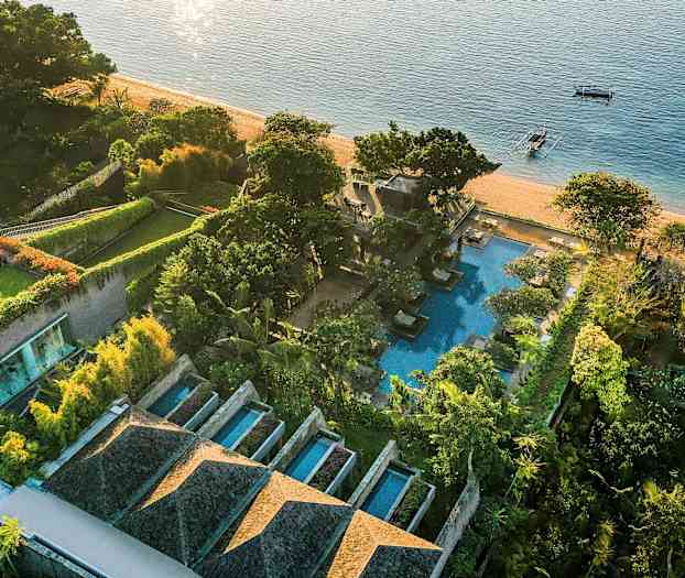 Et fugleperspektiv af et strandnært luksushotel med swimmingpools, grønne haver og stranden som grænser til havet. (AI-genereret tekst)