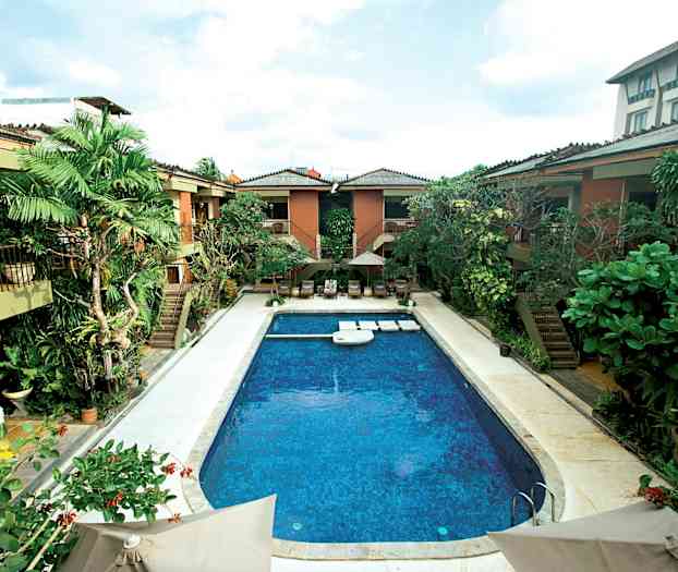 Billede af en udendørs pool omgivet af tropisk vegetation og bygninger. (AI-genereret tekst)