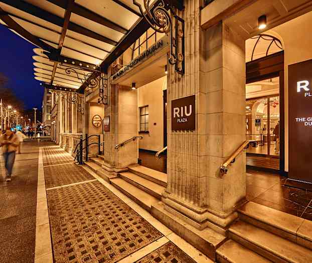 Hotel RIU Plaza Gresham Dublin indgang med oplyste skilte, aftenstemning. (AI-genereret tekst)
