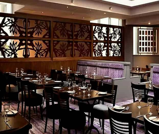 En stilfuld restaurant med borde og stole opstillet, en dekorativ væg med blomsterdesign og lilla detaljer på siddepladser. (AI-genereret tekst)