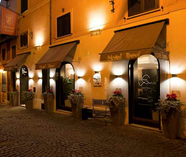 Hotelindgang med indbydende belysning, blomsterkrukker og skilte. (AI-genereret tekst)