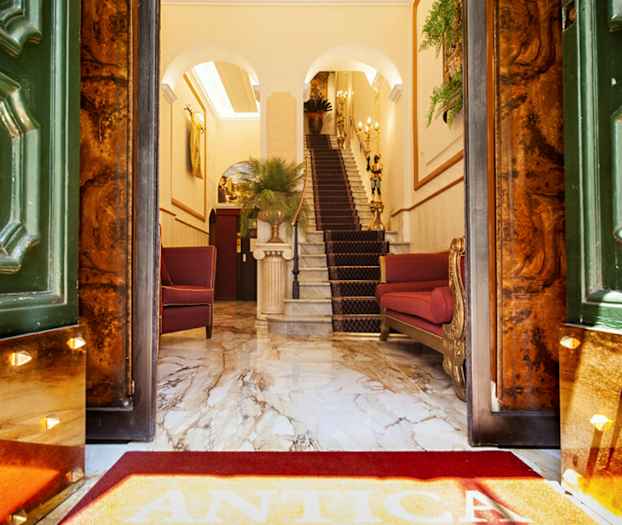 Indgang til elegant hotel med marmorgulv, røde stole og trappe. (AI-genereret tekst)