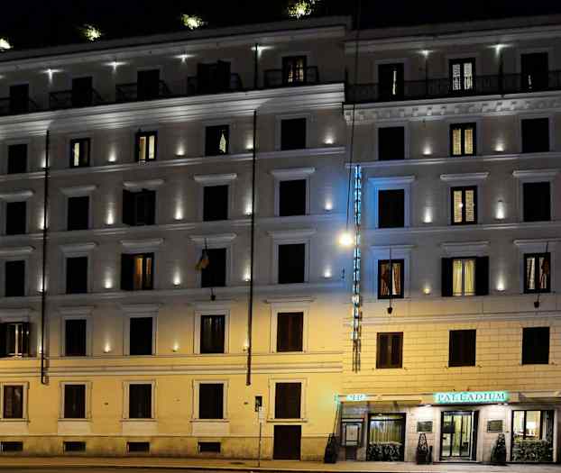 En flerbeboelsesejendom oplyst om aftenen med et hotelskilt og belyste vinduer. (AI-genereret tekst)