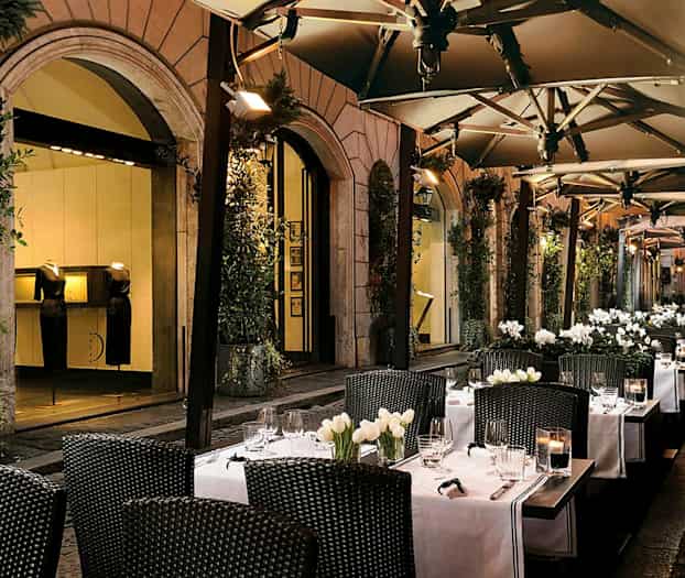 Udendørs servering med borde, hvide duge og blomsterdekorationer. (AI-genereret tekst)