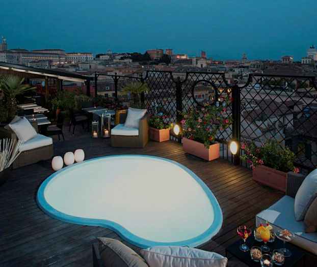 Billede af en tagterrasse med en lille pool og siddepladser samt udsigt over en by i skumringen. (AI-genereret tekst)