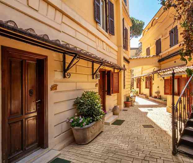 En solrig gårdhave med jordgule bygninger, trapper og blomsterplanter. (AI-genereret tekst)