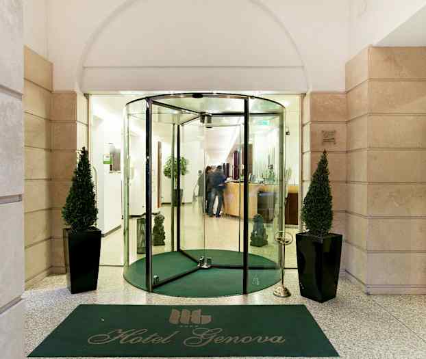 Indgangen til Hotel Genova med glasdøre, grøn måtte og to dekorerede planter. (AI-genereret tekst)