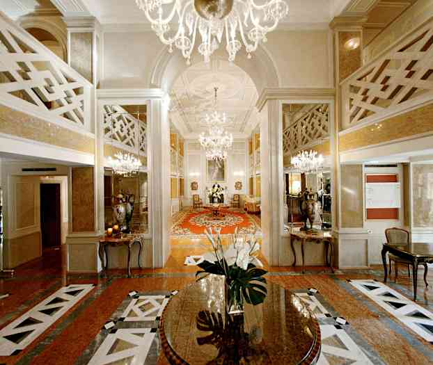 En elegant hotellobby med lysekroner, spejle og et centralt bord med blomster. (AI-genereret tekst)