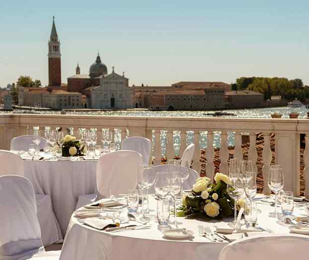 En udendørs middag på en terrasse med udsigt til en historisk bygning ved vandet. (AI-genereret tekst)