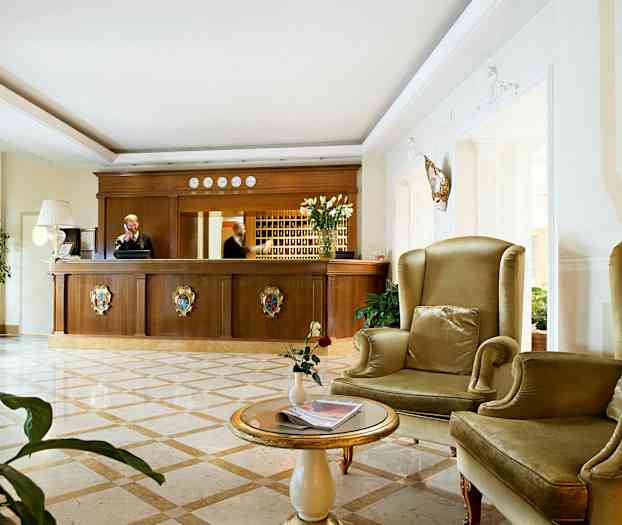 Et hotelreceptionsområde med en reception i træ og siddepladser med grønne lænestole. (AI-genereret tekst)