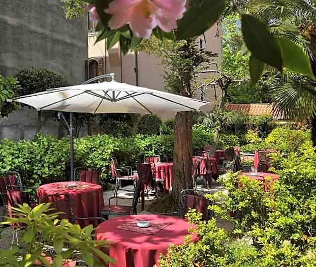 En frodig gårdhave med røde borde og stole samt en stor hvid parasol. (AI-genereret tekst)