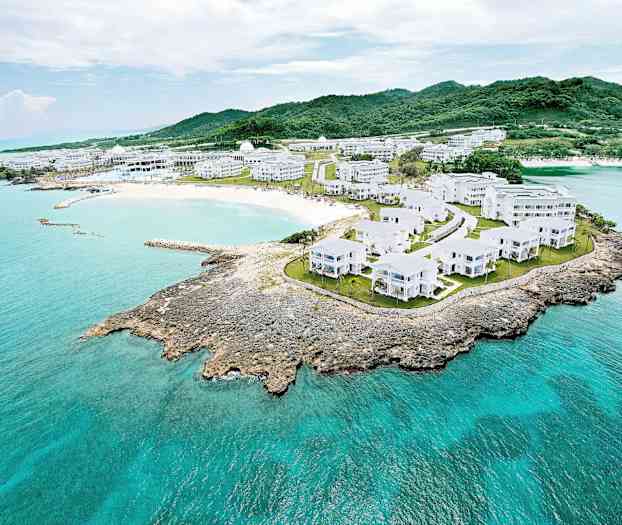 Luftfoto af et kystlandskab med hvide bygninger omgivet af grønne områder og turkisblåt vand. (AI-genereret tekst)