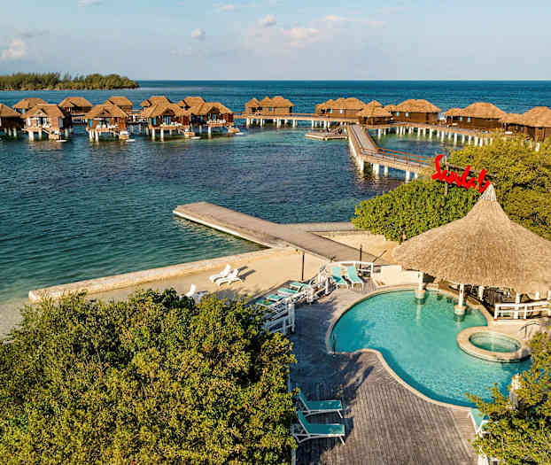 Flydende bungalows på stolper i havet med en pool og liggestole i forgrunden. (AI-genereret tekst)