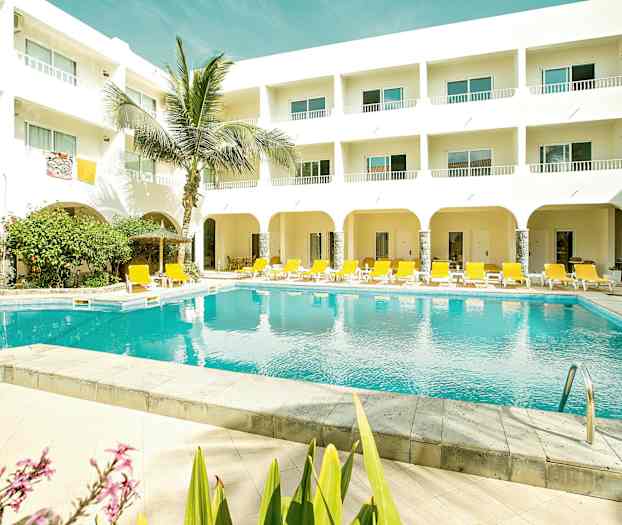 En udendørs pool med gule liggestole og en hvid bygning med altaner. (AI-genereret tekst)