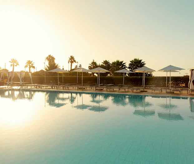 Poolområde med liggestole og parasoller ved solnedgang. (AI-genereret tekst)