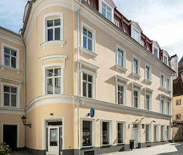 En beige bygning med hvide detaljer og rødt tag i et byområde. (AI-genereret tekst)