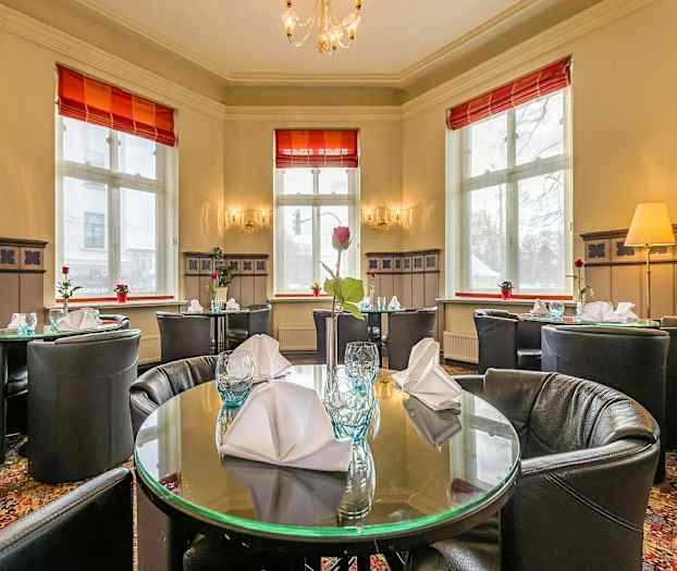 Interiør af en restaurant med dækkede, runde borde og store vinduer. (AI-genereret tekst)