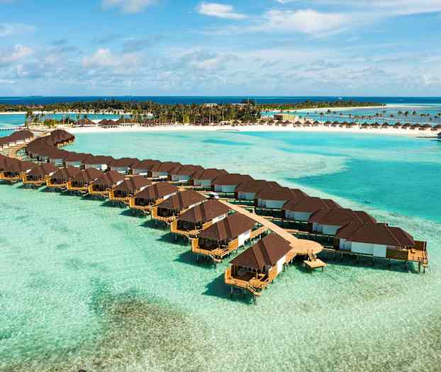 Bungalows over vand med en tropisk strand i baggrunden. (AI-genereret tekst)