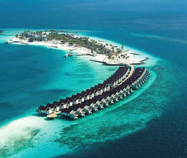 Luftfoto af en ø med strand, palmer og boliger bygget over vandet. (AI-genereret tekst)