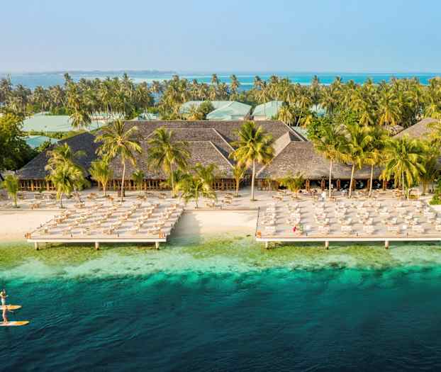 Hotelanlæg ved stranden med liggestole og turkisblåt vand. (AI-genereret tekst)