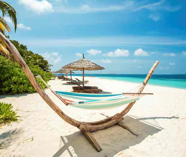 En strand med en hængekøje, parasoller og solsenge ved havet. (AI-genereret tekst)