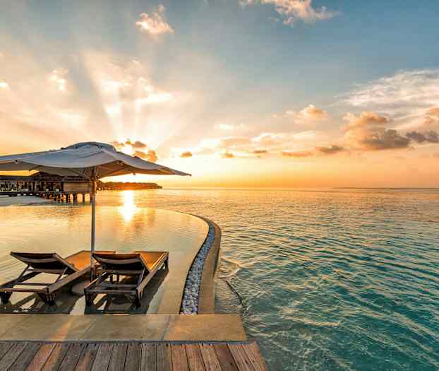 To liggestole med parasol ved en infinity-pool og havet i solnedgang. (AI-genereret tekst)