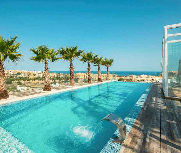 En infinitypool med udsigt over havet og byen, omgivet af palmer og trædæk. (AI-genereret tekst)