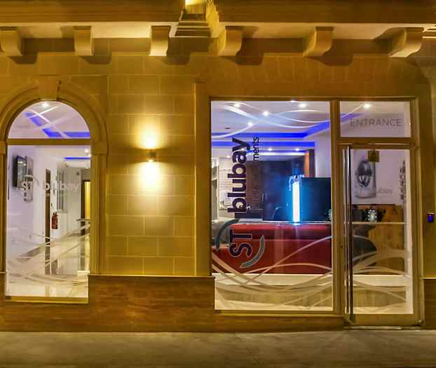 Indgangen til en bygning med glasvinduer og døre, oplyst om aftenen. (AI-genereret tekst)