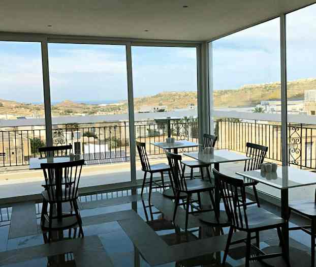 Et caféområde med store vinduer og udsigt til et landskab. (AI-genereret tekst)