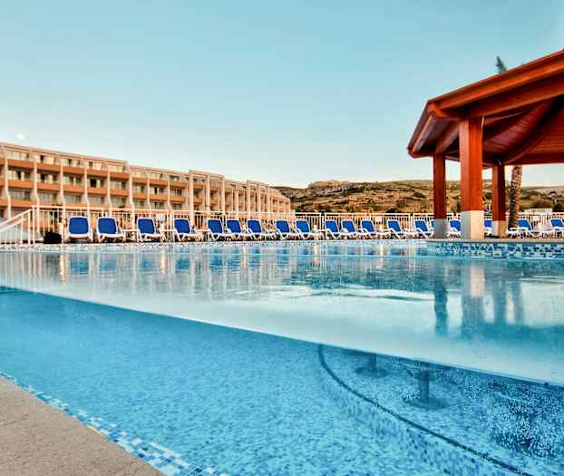 Udendørs swimmingpool med liggestole og hotelbygning i baggrunden. (AI-genereret tekst)