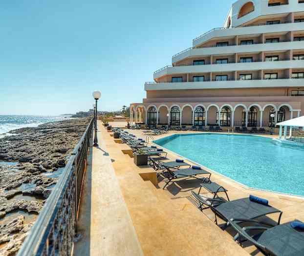 Billede af en luksuriøs ferieresort ved havet med en swimmingpool, solvogne og en bygning med altaner. (AI-genereret tekst)