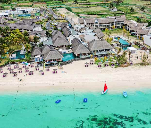 Luftfoto af en strand med liggestole, parasoller og et resort ved vandkanten. (AI-genereret tekst)