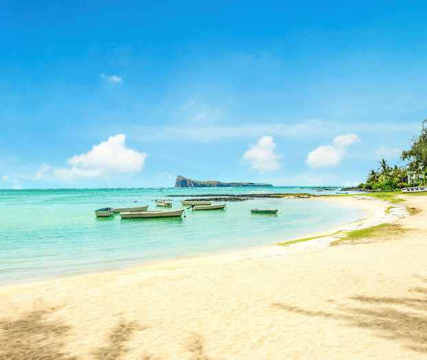 En sandstrand med småbåde i det klare vand og vegetation ved kanten. (AI-genereret tekst)