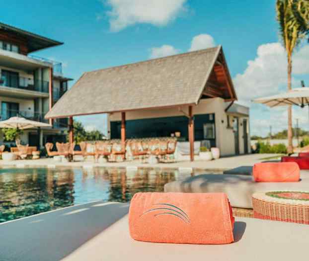 Poolområde med liggestole og en bygning i baggrunden. (AI-genereret tekst)