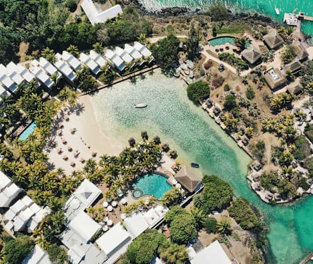 Luftfoto af et hotelområde med pool, en sandstrand og beplantning ved vandet. (AI-genereret tekst)