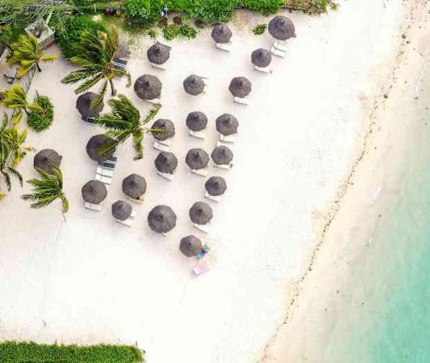 Luftfoto af en sandstrand med liggestole og parasoller tæt på vand og vegetation. (AI-genereret tekst)