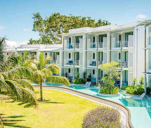 Et moderne feriehotel med hvide bygninger og altaner omgivet af en frodig have med tropiske planter. (AI-genereret tekst)